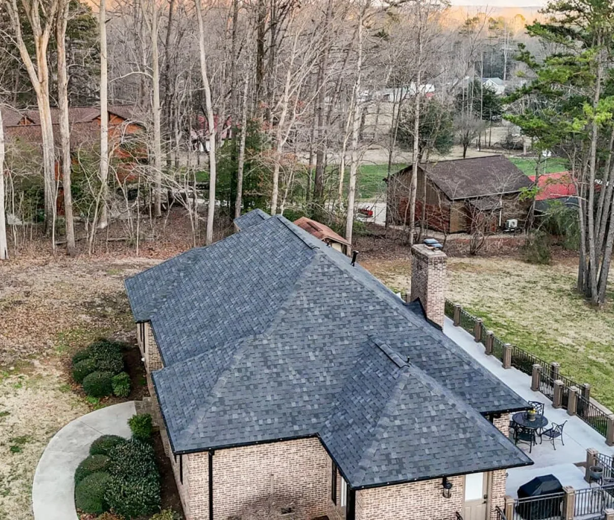 An aerial view of a brick house with a dark gray shingled roof